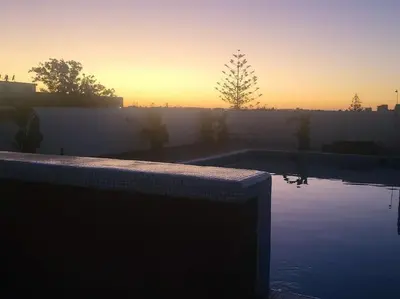 a swimming pool with a sunset in the background at Le Cocon d'Oasis - Location journalière Casablanca in Casablanca