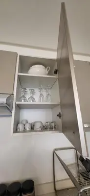 a white kitchen with glasses and dishes on shelves at Le Cocon d'Oasis - Location journalière Casablanca in Casablanca
