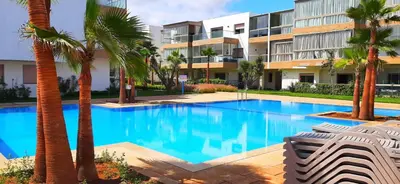 a swimming pool with palm trees in front of a building at Bleu Beach uniquement pour famille in Sidi Rahal