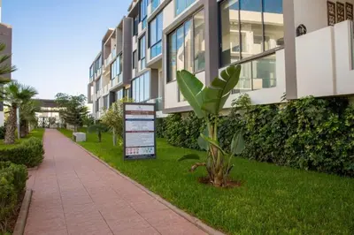 a building with a sign in the grass next to a sidewalk at Appartement - Dar Bouazza spacieux avec piscine à Dar Bouazza in Dar Bouazza