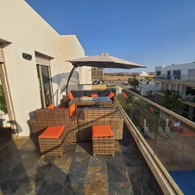 a patio with chairs and an umbrella on a balcony at Sidi Rahal Bleu Beach family in Sidi Rahal