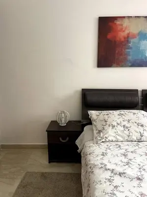 a bedroom with a bed with a nightstand and a painting at Luxury apartment 5 minutes Casablanca Airport in Nouaceur