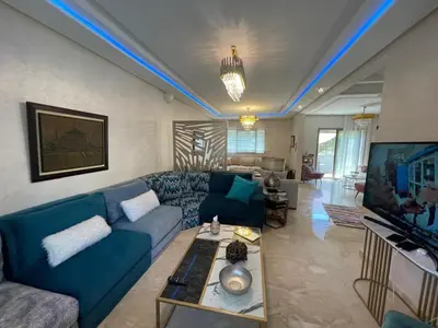 a living room with a blue couch and a tv at BEAU TRIPLEX EN RESIDENCE in Skhirat