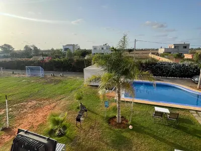 a man standing next to a palm tree next to a pool at Villa avec piscine et jardin privés in Casablanca