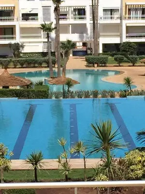 a large swimming pool with palm trees and a building at Appartement meublé piscine Residence eden tamaris in Dar Bouazza