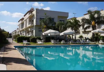 a swimming pool in front of a hotel at OASIS BEACH APPARTEMENT MEUBLé RESIDENCE FERMÉE AVEC PISCINE TAMARIS 2 SIDI RAHAL in Sidi Rahal