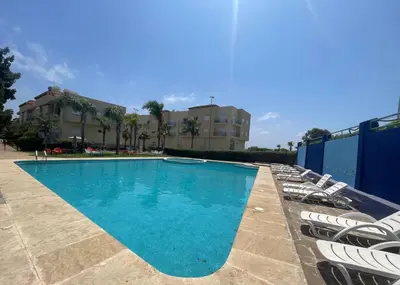 a swimming pool with chairs and a building in the background at OASIS BEACH APPARTEMENT MEUBLé RESIDENCE FERMÉE AVEC PISCINE TAMARIS 2 SIDI RAHAL in Sidi Rahal