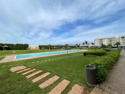 a swimming pool with a trash can in the grass at Superbe Appt avec grande piscine 2 in Dar Bouazza