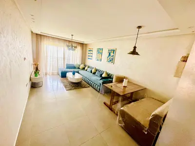 a living room with a blue couch and a table at Appartement Cozy avec piscine in Sidi Rahal