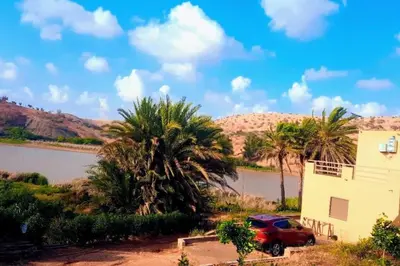 a red car parked next to a building and palm trees at Lake House Boulaouane in El Jadida