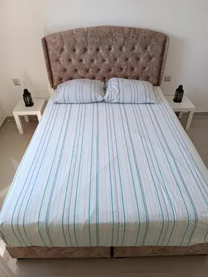a bed with a blue and white striped comforter and two tables at Appartement avec piscine à Mohammedia Plage à 5min in Mohammedia