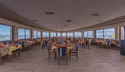 a dining room with tables and chairs and windows at Hotel Tropicana in Casablanca