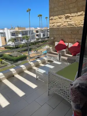 a balcony with chairs and a table with red pillows at Eden tamaris résidence in Dar Bouazza
