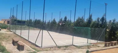 a net on a tennis court with a basketball hoop at Ferme d'hôte Evasio in Sidi Rahal
