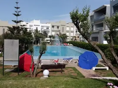 a swimming pool with umbrellas in front of a building at Appartement Luxueux vue Mer dans Résidence avec piscines et jardin in Dar Bouazza
