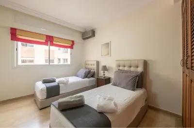a bedroom with two beds and a couch and a window at Cosy Apartment 200 M2 Hay Ryad Rabat in Rabat