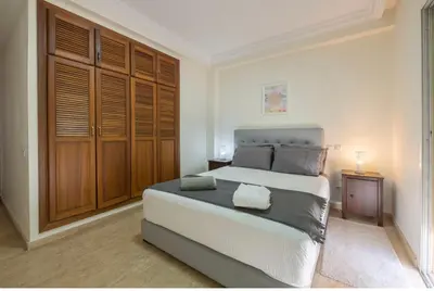 a bedroom with a large bed and wooden cabinets at Cosy Apartment 200 M2 Hay Ryad Rabat in Rabat