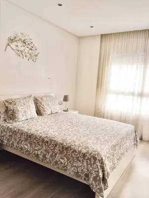 a white bedroom with a large bed and a window at Appartement Cozy au Triangle d’or in Casablanca