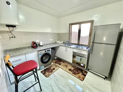 a kitchen with a refrigerator and a red chair at A3 Luxe and Cosy Apartement, 7 min du Stade Moulay Abdellah in Temara