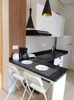 a kitchen with a black counter with two white chairs at Studio à Prestigia HayRiad/Rabat in Rabat
