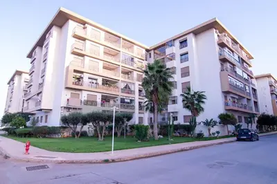 a large white apartment building with palm trees and a fire hydrant at New Luxury apartment 5 min Casablanca Mohammed V Airport in Casablanca