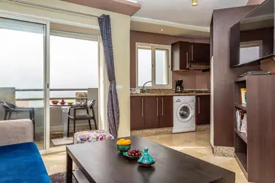 a living room with a table and a kitchen with a view at Appartement Panoramique in Casablanca