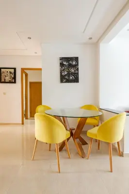 a dining room with a glass table and yellow chairs at New Luxurious apartment Agdal Rabat center in Rabat