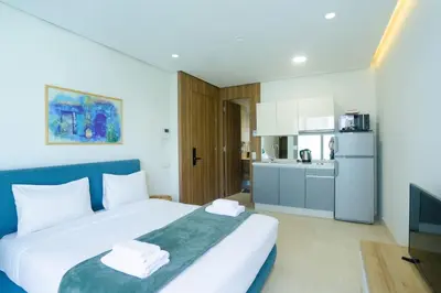 a bedroom with a large white bed and a kitchen at Résidence Ronomo - Racine in Casablanca