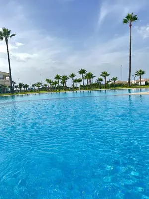 a large pool of blue water with palm trees at Appartement Moderne à OlaBlanca2 in Sidi Rahal