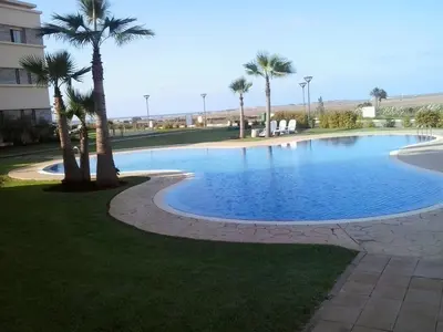 a large swimming pool with palm trees in front of a building at Appartement Bella Vista in Bouznika