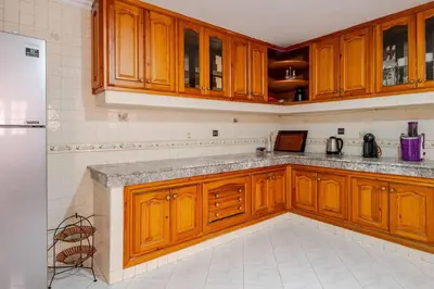 a kitchen with wooden cabinets and a white tile floor at Spacious Harhoura Villa: Perfect for Families (5min to Beach) in El Harhoura