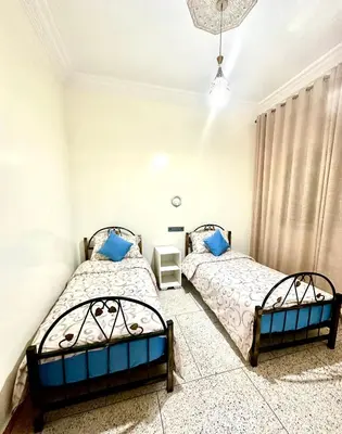 two beds in a bedroom with white walls and blue pillows at Jolie Appt à skhirat 5min de la plage par voiture in Skhirat