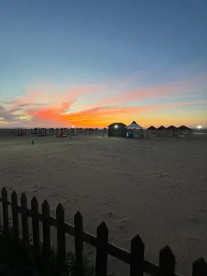 a sunset on the beach with tents and a fence at CASA BAY BEACH OMK 3 in Sidi Rahal