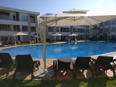 a group of chairs and an umbrella next to a pool at My Cosy Place - Apartment 2BR - Piscine - Bahia Beach - Bouznika in Bouznika