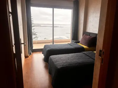 two beds in a room with a large window at Appartement vue sur mer résidence Les vagues des sablettes Mansouria in Mohammedia