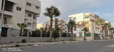 an empty street with palm trees in front of buildings at Appartement Proche plage Bouznika Bouznika in Bouznika