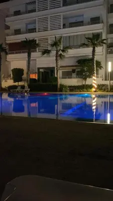 a swimming pool with palm trees in front of a building at Résidence Balnéaire, Appartement 2 Chambres in Mansouria