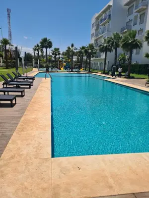 a large swimming pool with chairs and a building at Appartement résidence kettani jardin privatif accès direct piscine et aire de jeu in Bouznika