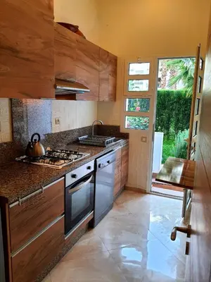 a kitchen with wooden cabinets and a stove top oven at Appartement résidence kettani jardin privatif accès direct piscine et aire de jeu in Bouznika