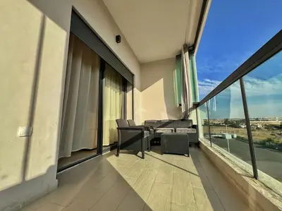 a balcony with chairs and a table and windows at Séjour Chic - Appartement Moderne avec Piscine in Bouznika