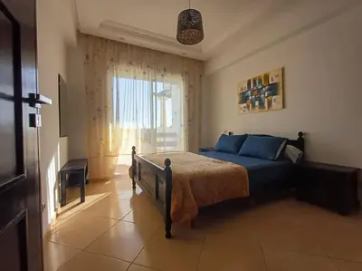 a bedroom with a bed with blue pillows and a window at Appartement Sidi Rahal à Garden beach2 in Sidi Rahal