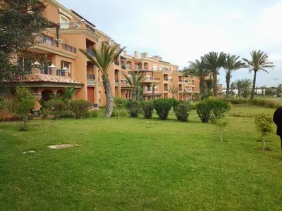 a large apartment building with palm trees in a park at Appartement de H standing in Bouznika