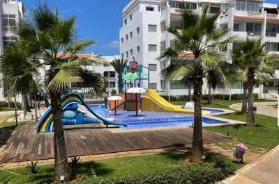 a playground with a slide in a park with palm trees at La siesta beach resort two bedroom appartement in Mohammedia