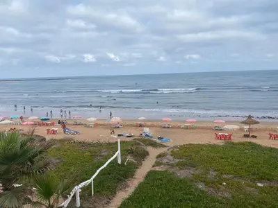 a beach with people and umbrellas and the ocean at Maison d'hôte sur la Plage de Bouznika in Bouznika