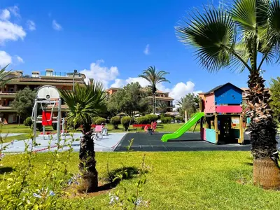 a playground with a slide in a park with palm trees at Appartement de plain-pied, piscine et mer in Bouznika