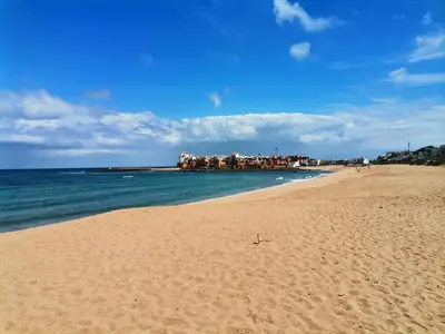 a sandy beach with buildings in the distance and the ocean at Grand appartement vue golf a 2 min de la plage Bouznika in Bouznika