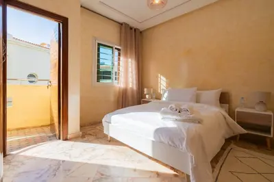 a bedroom with a white bed and a large window at Maison avec Piscine Proche Plage in El Harhoura