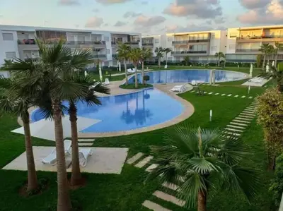 an empty swimming pool with palm trees in front of a building at Appartement Sidi Rahal in Berrechid