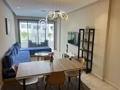 a living room with a table and a blue couch at Cozy New Apartment in Tamaris in Dar Bouazza