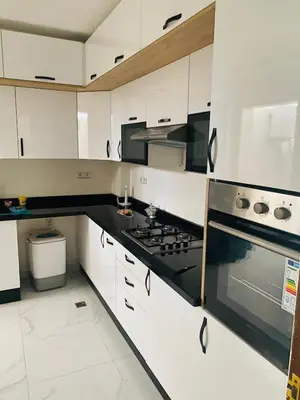 a kitchen with white cabinets and black appliances at harhoura Résidence Badia in Temara